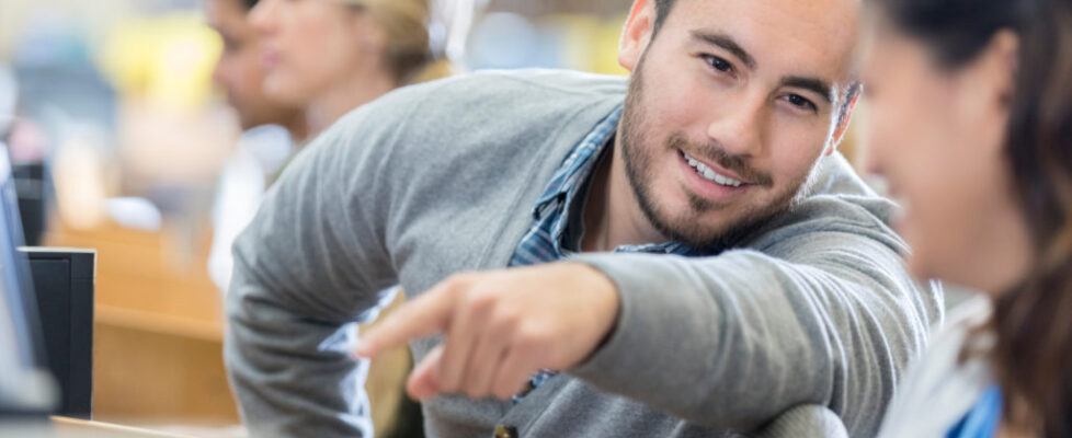 Male college student helps classmate in computer lab